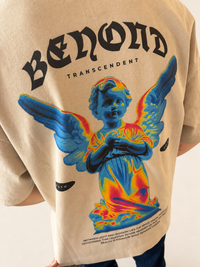A close-up of a beige t-shirt featuring a large graphic print of a blue angel with colorful neon-like wings and the text 'BENON TRANSCENDENT' on the back.
