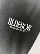 Close-up of a black fabric surface with white printed text reading 'BLUESOR' and smaller text 'MEMBERS' SOCIETY'.
