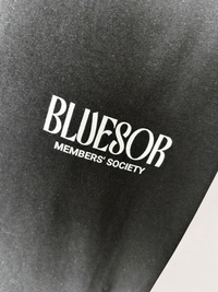 Close-up of a black fabric surface with white printed text reading 'BLUESOR' and smaller text 'MEMBERS' SOCIETY'.