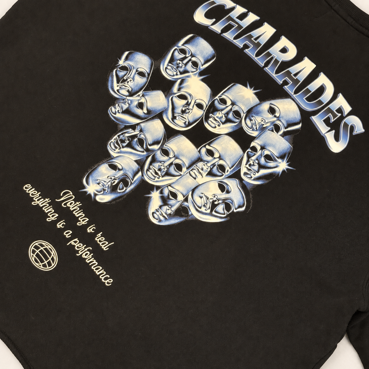 Close-up of a black graphic T-shirt featuring the word 'CHARADES' in large metallic silver letters above a cluster of stylized silver skulls, with smaller white text reading 'Nothing is real everything is a performance' and a small globe logo.