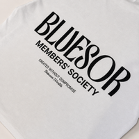 White t-shirt featuring a bold black graphic print on the front that reads 'BLUESOR MEMBERS' SOCIETY' with smaller text 'CREATED WITHOUT COMPROMISE Between Us'.