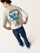 A man wearing a cream-colored Beyond brand t-shirt with a large colorful angel graphic on the back, paired with dark blue jeans and white sneakers, photographed from behind against a light studio background.