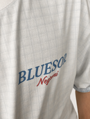 Close-up of a light gray plaid short-sleeve t-shirt featuring the text 'BLUESOR' in blue and 'Negrí' in red on the chest.