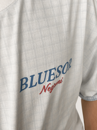 Close-up of a light gray plaid short-sleeve t-shirt featuring the text 'BLUESOR' in blue and 'Negrí' in red on the chest.